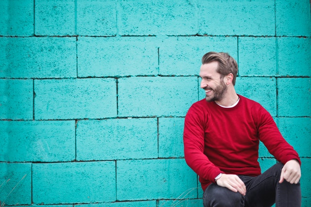 Muž v červenom svetri sediaci pred tyrkysovou stenou
